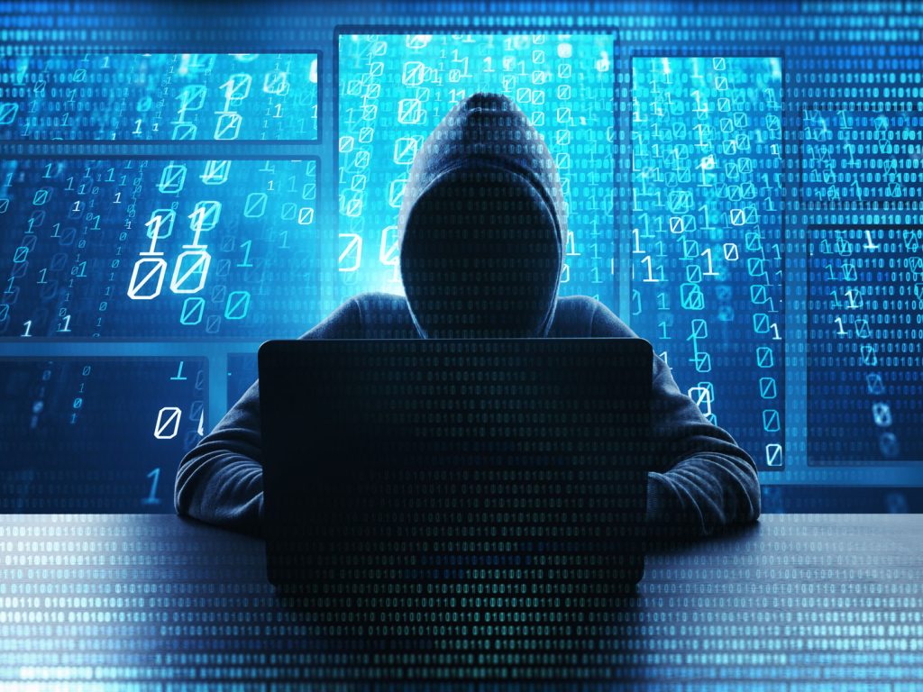 Hacker sitzt vor einem Laptop, mit Zahlencodes im Vordergrund, versucht Privileged Access Management zu umgehen.